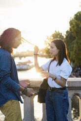 France, Paris, young couple standing on a bridge at river Seine at sunset - AFVF01130