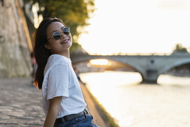 France, Paris, portrait of smiling young woman with sunglasses at river Seine at sunset - AFVF01142