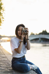 Frankreich, Paris, Porträt einer jungen Frau mit Kamera am Fluss Seine bei Sonnenuntergang - AFVF01147