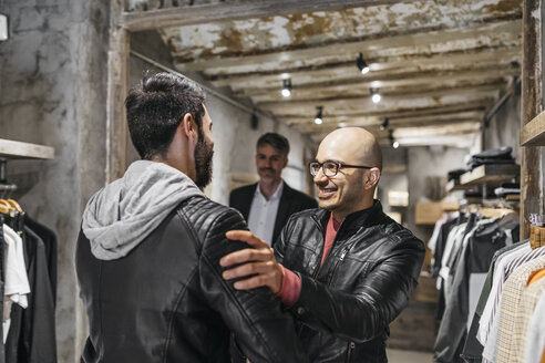 Zwei lächelnde Männer treffen sich in einem modernen Herrenbekleidungsgeschäft - JRFF01698