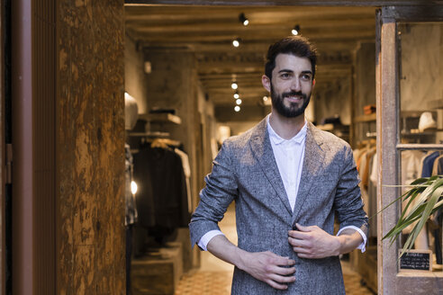 Porträt eines lächelnden Mannes mit Jacke, der ein Herrenbekleidungsgeschäft verlässt - JRFF01710