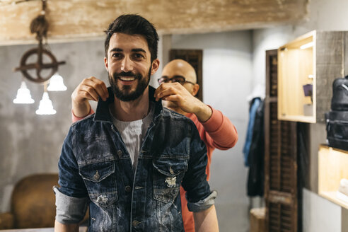 Handsome man trying on new denim jacket with stylist in modern boutique - JRFF01714