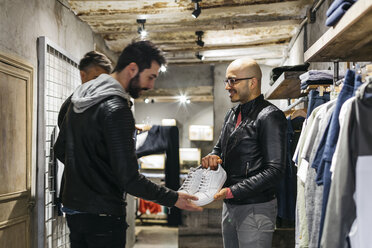 Designer in modern menswear shop showing new shoes to man - JRFF01718