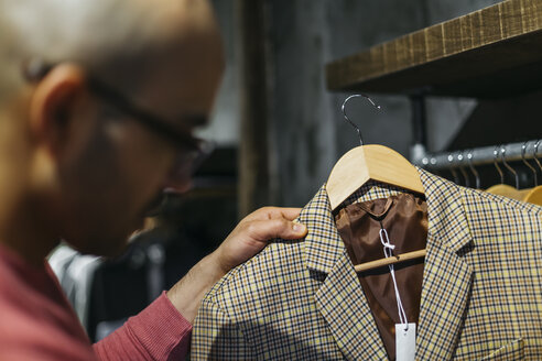 Mann betrachtet eine Jacke in einem Herrenbekleidungsgeschäft - JRFF01719