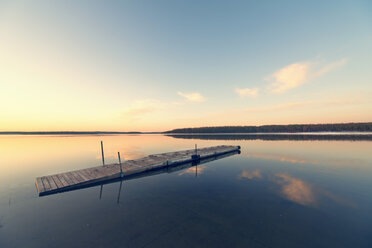 A wooden dock floating on flat calm waters of a lake at sunset. - MINF02883