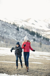 Ein Bruder und eine Schwester, die im Winter gemeinsam über die Wiese rennen. - MINF02891