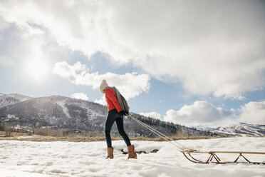 Ein junges Mädchen in einer roten Jacke, das einen leeren Schlitten durch den Schnee zieht. - MINF02897