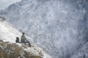 A man, a hiker in the mountains, taking a rest on a rock outcrop above a valley. - MINF02906