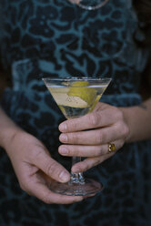 A woman holding a martini glass with a cocktail and a twist of lemon peel. - MINF02919