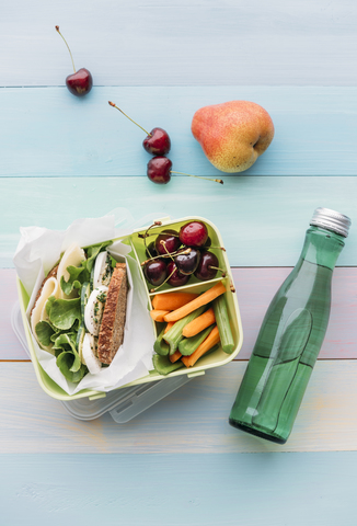 Healthy school food in a lunch box, vegetarian sandwich with cheese, lettuce, cucumber, egg and cress, sliced carrot and celery, cherries and pear stock photo