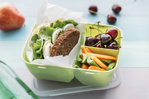 Gesundes Schulessen in der Lunchbox, vegetarisches Sandwich mit Käse, Salat, Gurke, Ei und Kresse, Karotten- und Selleriescheiben, Kirschen und Birne, lizenzfreies Stockfoto