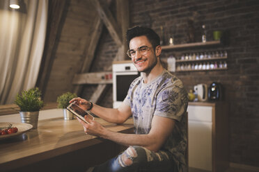 Portrait of smiling young man using tablet in kitchen at home - AWF00125