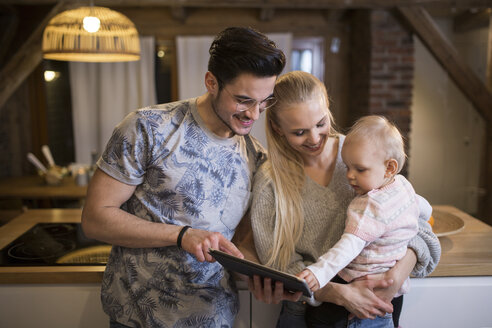 Glückliche junge Eltern nutzen das Tablet zu Hause mit ihrem kleinen Mädchen - AWF00129