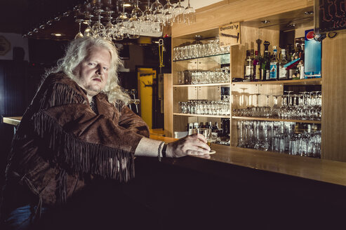 Portrait of blond rocker wearing brown leather jacket standing at counter of an old-fashioned pub - FRF00701