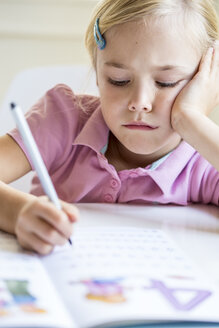 Porträt eines gelangweilten kleinen Mädchens, das Zahlen in ein Schulheft schreibt - JFEF00895