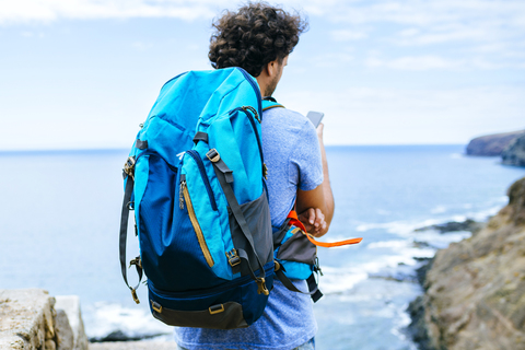 Spanien, Kanarische Inseln, Gran Canaria, Nahaufnahme eines Mannes mit Rucksack, der ein Mobiltelefon benutzt, lizenzfreies Stockfoto