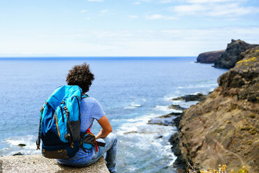 Spanien, Kanarische Inseln, Gran Canaria, Mann mit Rucksack auf Felsen sitzend - KIJF01975