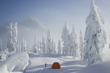 Ein leuchtend orangefarbenes Zelt steht auf einem verschneiten Bergrücken mit Blick auf einen Berg in der Ferne. - MINF02935