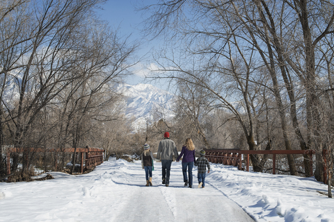 Winterlandschaft mit Schnee auf dem Boden. Eine Familie, Erwachsene und zwei Kinder, geht eine leere Straße entlang., lizenzfreies Stockfoto