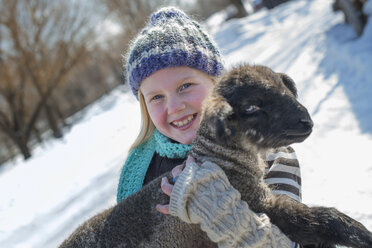 Winter scenery with snow on the ground. A young girl holding a young lamb. - MINF02951