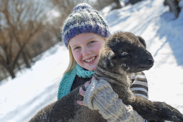 Winterlandschaft mit Schnee auf dem Boden, ein junges Mädchen hält ein junges Schaf. - MINF02951