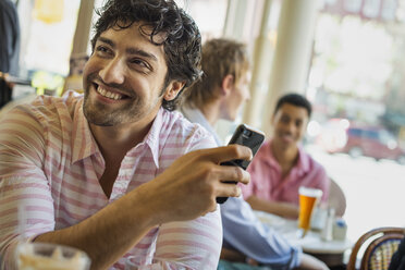 Urbaner Lebensstil: Drei junge Männer an einem Tisch in einem Café. Einer benutzt sein Smartphone - MINF02959