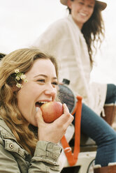 Zwei junge Frauen, eine beißt in einen Apfel. - MINF02975