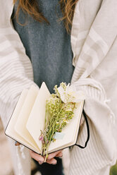 Nahaufnahme einer Frau, die ein Notizbuch in der Hand hält, zwischen dessen Seiten Wildblumen liegen. - MINF02988