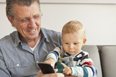 Mann mit Enkel, der ein Mobiltelefon benutzt - ISF17936