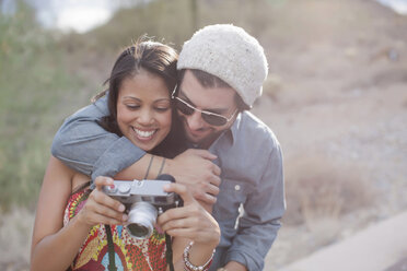 Couple embracing and holding camera on road trip, smiling - ISF18025