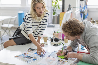 Young colleagues discussing photographs in meeting in creative office - ISF18047