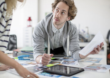 Young man using digital tablet and holding paper in creative office - ISF18049