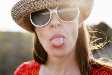 Mature woman wearing sunglasses and sunhat sticking out tongue - ISF18175