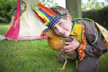 Junge im Indianerkostüm, der ein Huhn hält, Porträt - ISF18216