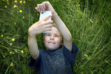 Boy lying on grass taking self portrait photograph using smartphone - ISF18234