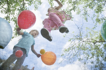 Young girls jumping on garden trampoline with balloons - ISF18249