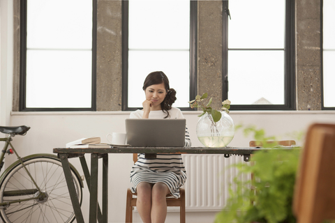 Junge Frau sitzt am Tisch mit Computer, lizenzfreies Stockfoto