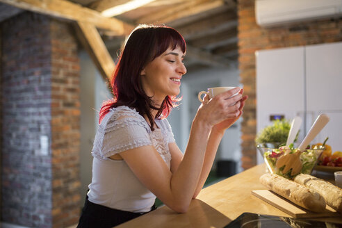 Lächelnde Frau trinkt eine Tasse Kaffee in der Küche zu Hause - AWF00157