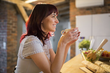 Smiling woman drinking cup of coffee in kitchen at home - AWF00158