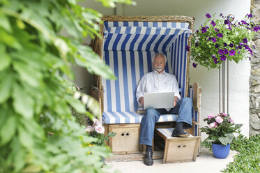 Älterer Mann benutzt Laptop auf Gartensitzplatz - ISF18479