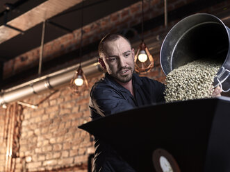 Mann gießt grüne Kaffeebohnen in Kaffeeröster - CVF01028