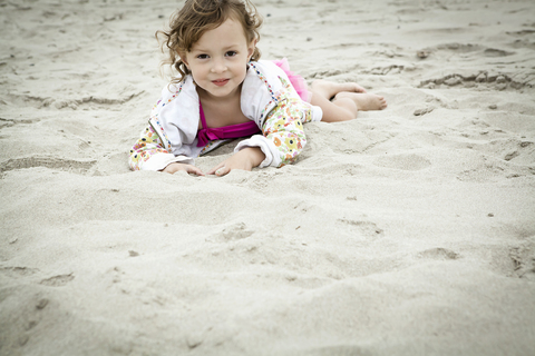 Porträt eines weiblichen Kleinkindes, das im Sand liegt, lizenzfreies Stockfoto