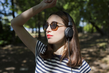 Porträt einer jungen Frau mit Sonnenbrille, die mit Kopfhörern Musik hört - GIOF04051