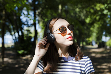 Portrait of young woman wearing sunglasses listening music with headphones - GIOF04053