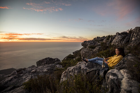 Südafrika, Kapstadt, Tafelberg, Frau sitzt auf einem Felsen und trinkt Wein bei Sonnenuntergang - DAWF00686