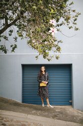 Woman wearing multicolored dress standing at garage door - DAWF00694