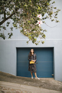 Woman wearing multicolored dress standing at garage door - DAWF00694