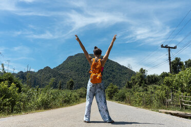 Laos, Vang Vieng, woman standing on country road with raised arms - AFVF01153