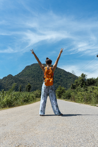 Laos, Vang Vieng, Frau auf Landstraße stehend mit erhobenen Armen, lizenzfreies Stockfoto