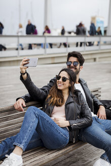 Spanien, Barcelona, glückliches junges Paar, das sich auf einer Bank ausruht und ein Selfie macht - MAUF01555